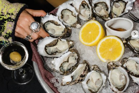 Hand reaching for an oyster from a tray of seafood with lemons.