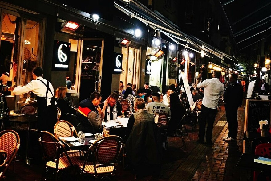 Restaurant exterior with awnings, waiters and customers at tables.