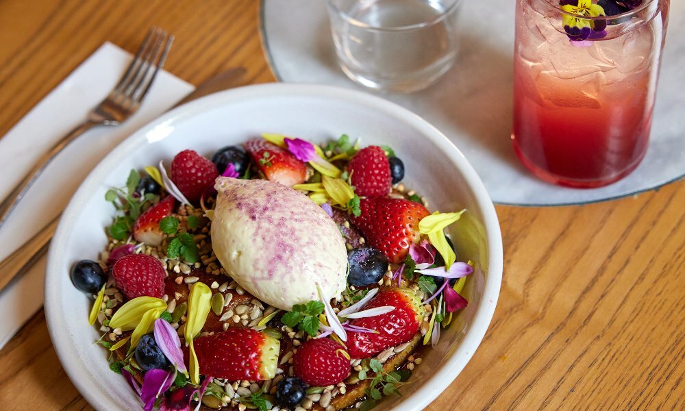 A fruit and cream topped breakfast and a pink beverage.