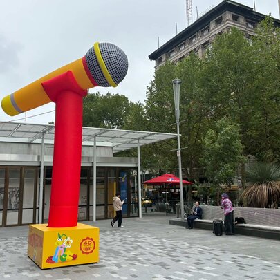 Huge Comedy Festival microphone prop in a paved courtyard with seating.