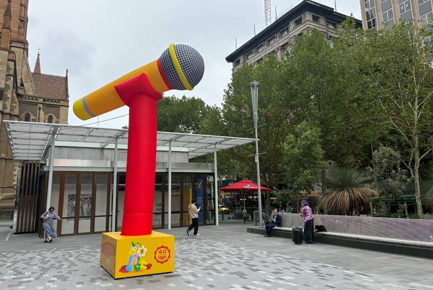 Huge Comedy Festival microphone prop in a paved courtyard with seating.