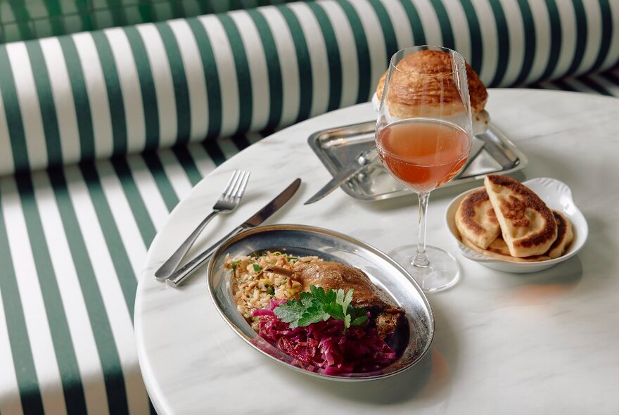 A selection of Asian  dishes, a side dish of roti, plus a drink on a table, with a green and white striped banquette in the background.