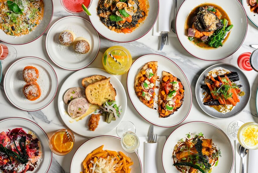 An array of plates with Italian food such as pizza, bruschetta and pasta, seen from above.