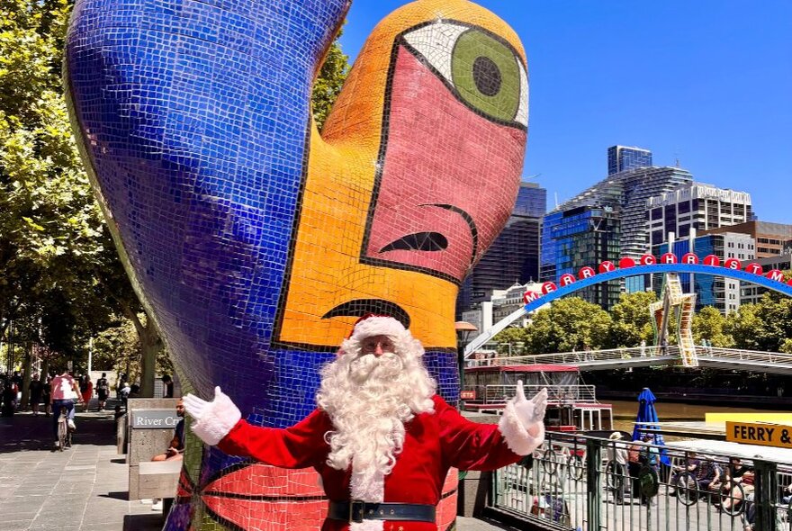 Santa standing in front of a mosaic outdoor sculpture on Southbank.