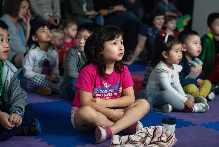 A group of children seated on the floor at the Immigration Museum, listening to a story time sesson.