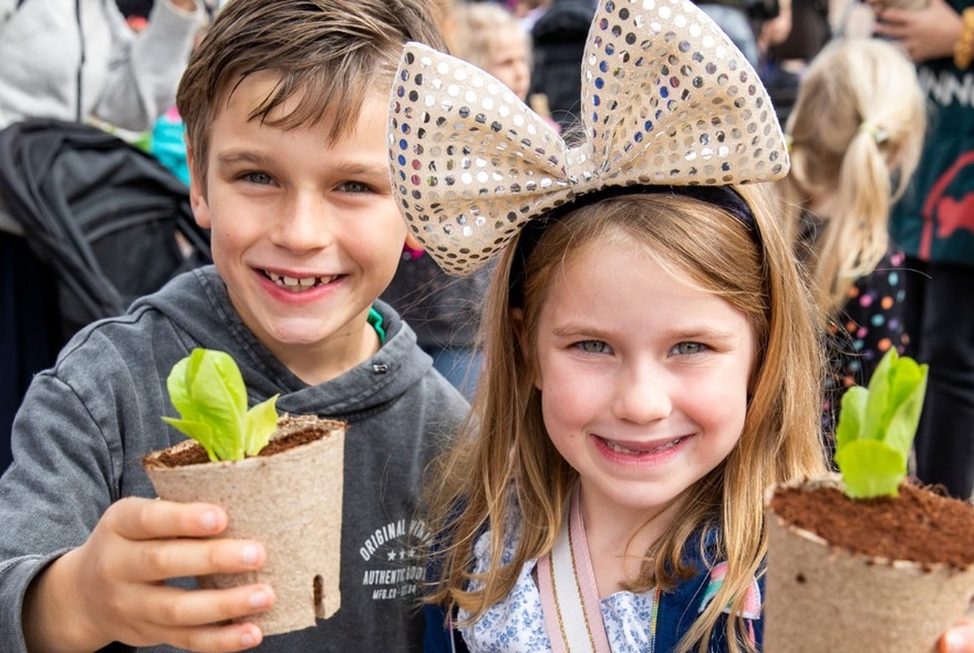 Two children smiling and holding up potted seedlings.