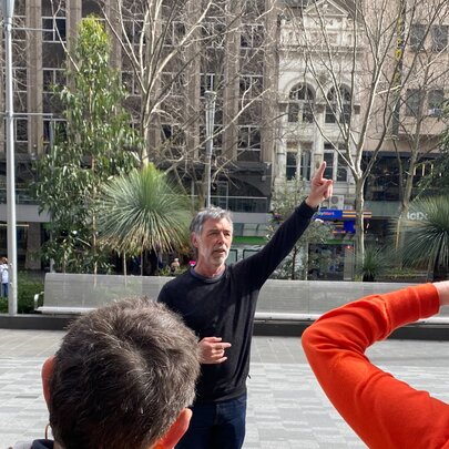 A tour guide with his hand in the air working in Melbourne's City Square.
