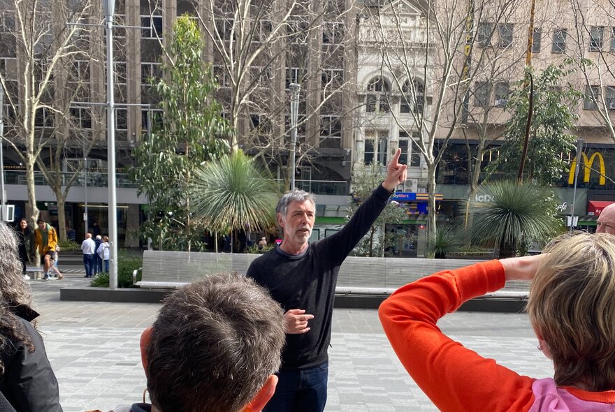 A tour guide with his hand in the air working in Melbourne's City Square.