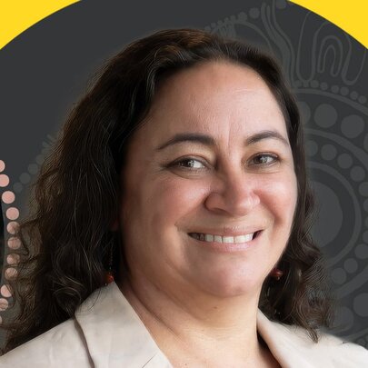 Headshot of a smiling woman with dark, curly hair wearing a light-colored blazer, positioned in front of a background that includes a yellow circular motif.