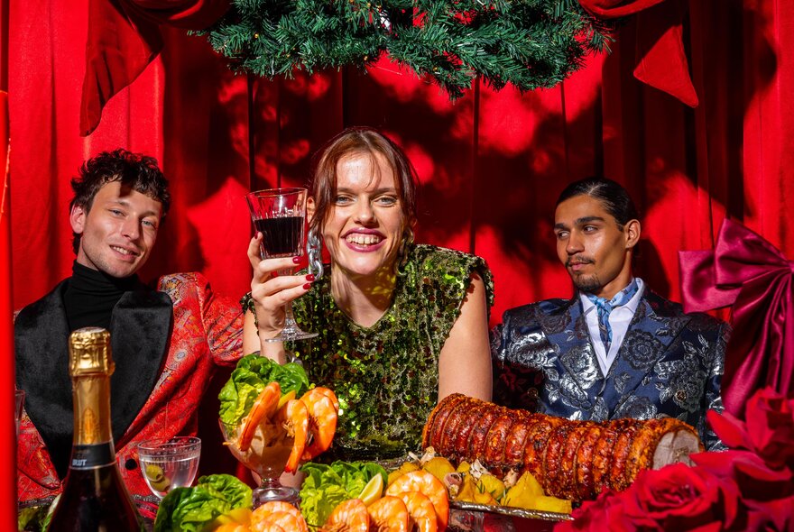 People looking happy in front of a Christmas feast, the woman raising a glass of red wine. 