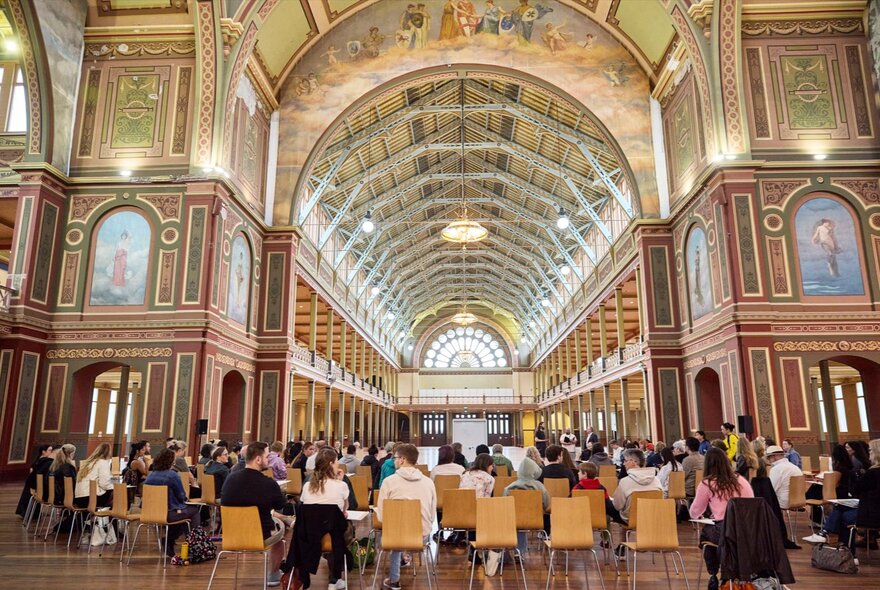 People seated in chairs in the great exhibition space in the Royal Exhibition Building, Melbourne.