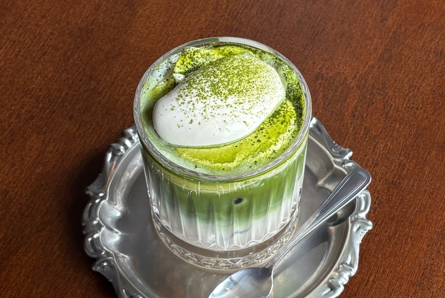 Cream-topped matcha drink on a silver tray with a spoon.