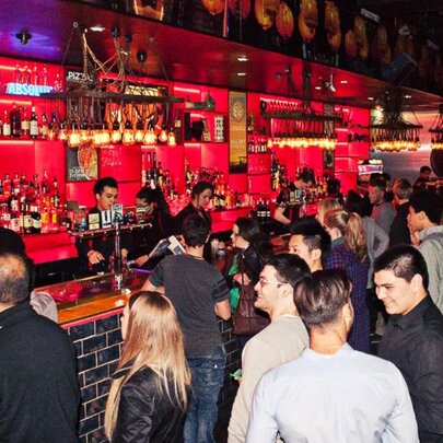 People milling around a bar that's illuminated with red lights. 