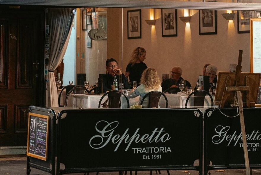 Diners in a small restaurant with Geppetto Trattoria barriers around the tables.