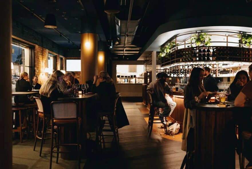 Interior of Central Club Hotel showing curved art-deco bar, soft lighting and patrons eating and drinking at high bench tables and the bar area.