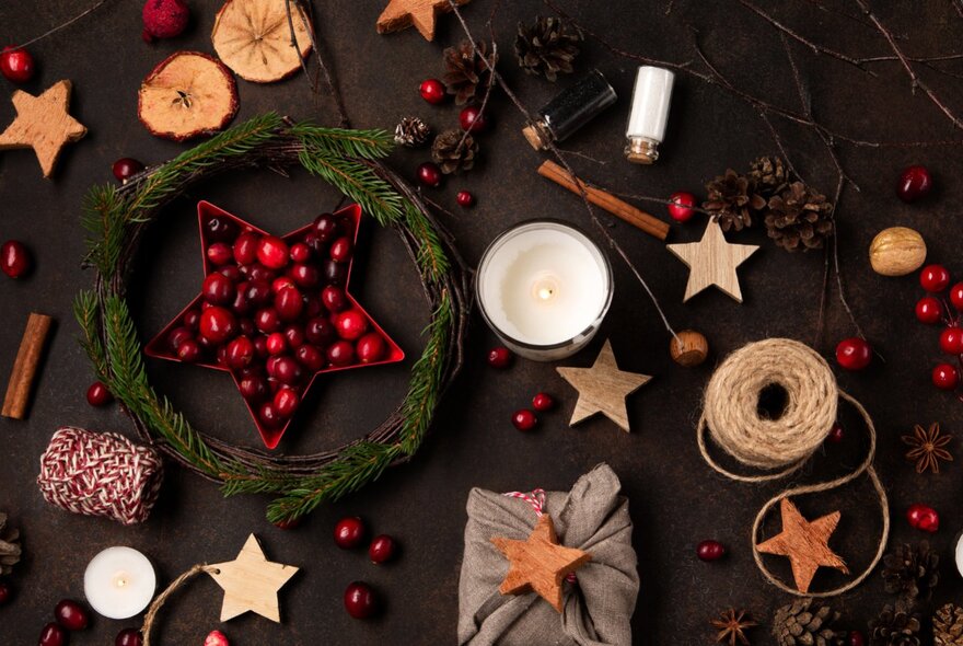 Looking down at a table of festive items including holly, a Christmas wreath, a candle, stars, and brown string. 