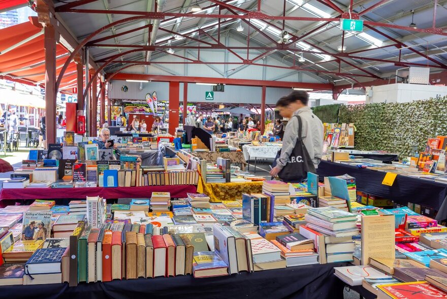 People browsing tables of books in a market shed.