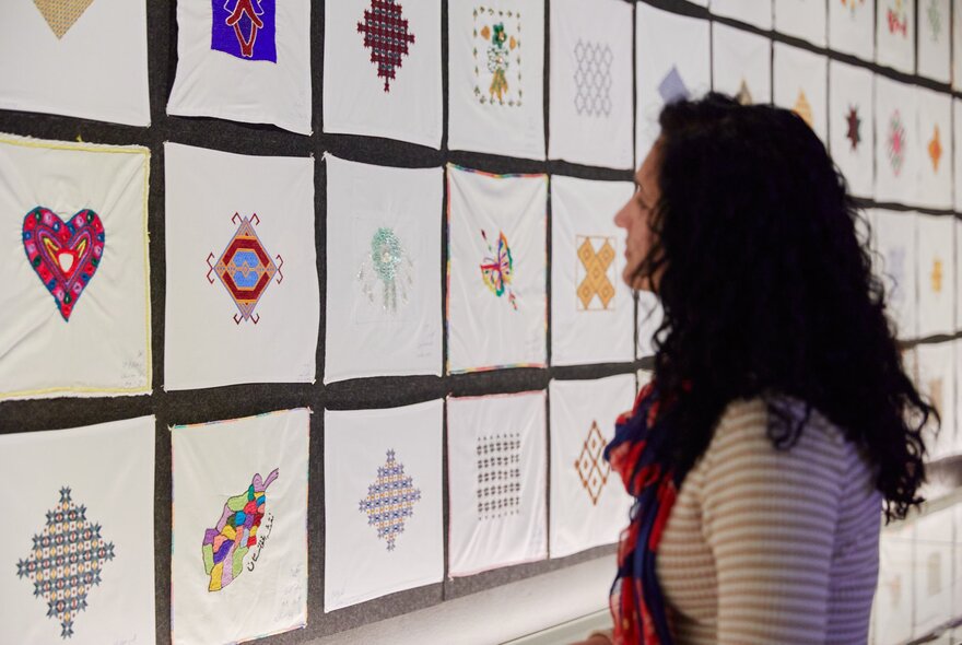 A woman looking at gallery exhibition of small white square embroidered handkerchiefs. 