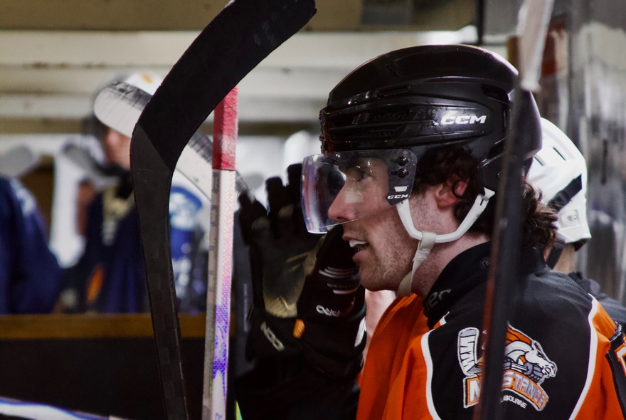 An ice hockey player wearing a Melbourne Mustangs jersey and a helmet on the bench.