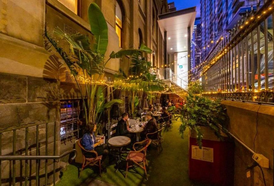 People sitting in the courtyard at a bar beneath fairy lights