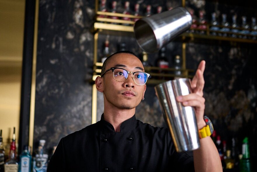 A bartender standing behind a bar and flipping a cocktail shaker.