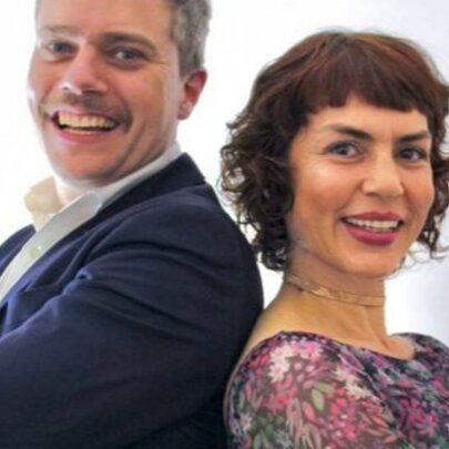 Singers Jackie Bornstein and Jeremy Hopkins standing back to back with arms crossed, smiling.