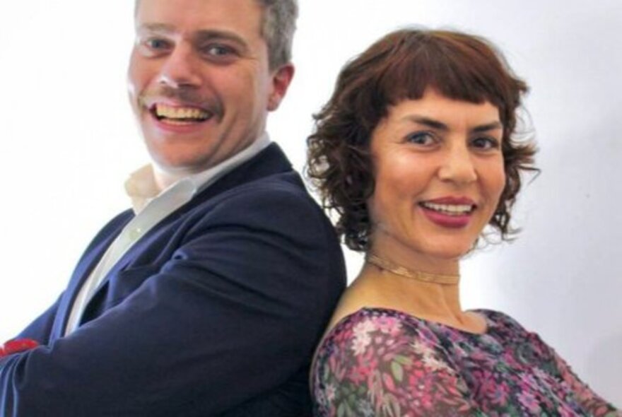 Singers Jackie Bornstein and Jeremy Hopkins standing back to back with arms crossed, smiling.