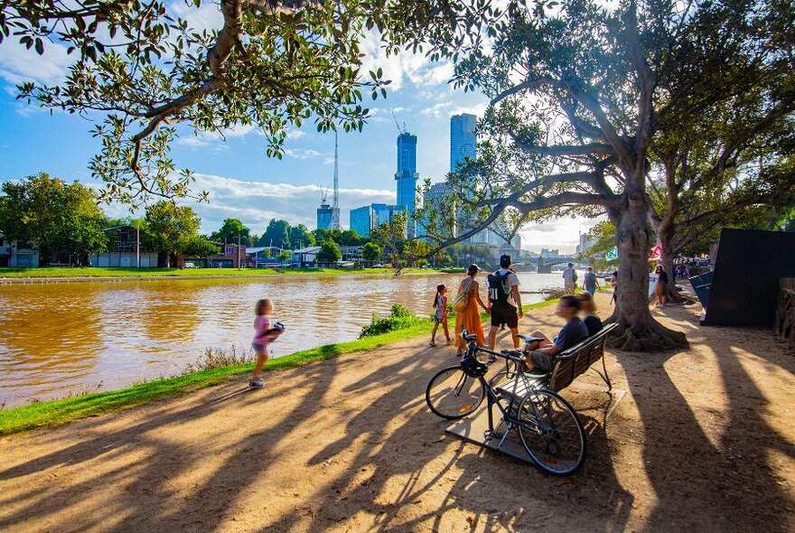 People walking along a dirt path on the banks of a city river.