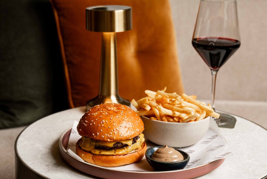 A fancy burger with fries and a glass of red wine. 