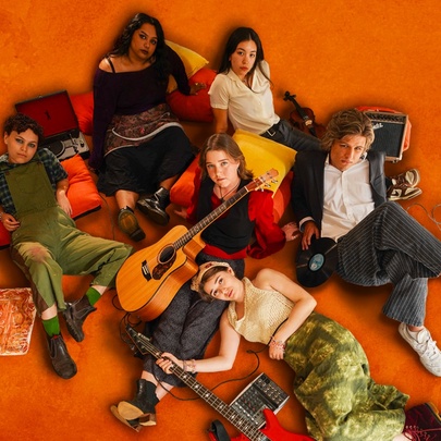 Group of young people lying on an orange floor with cushions and guitar.