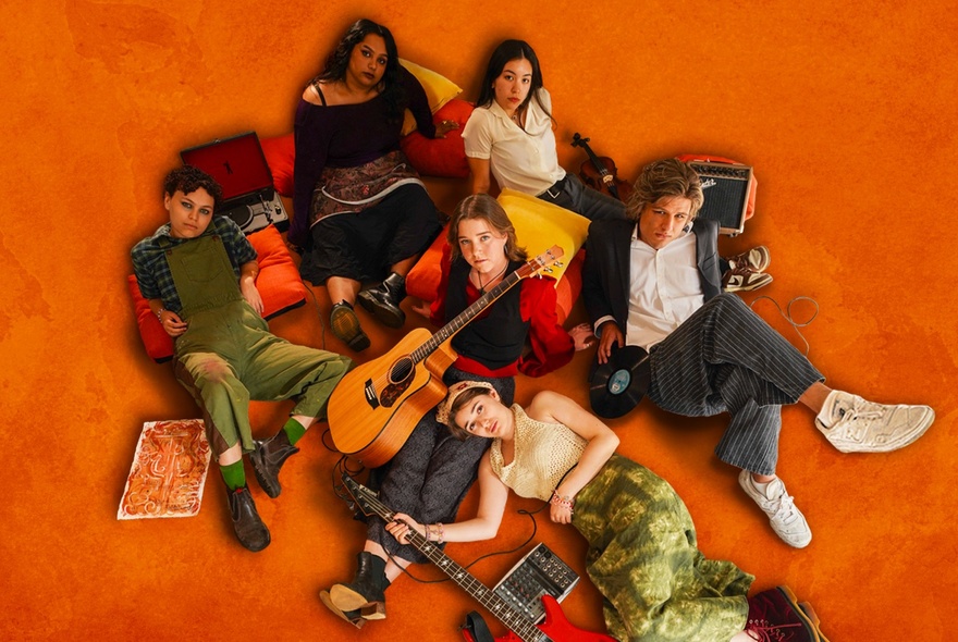 Group of young people lying on an orange floor with cushions and guitar.