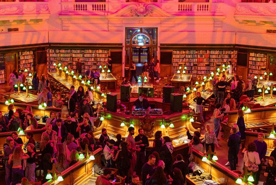 Interior of the State Library at night with lights and projections and people assembled casually. 