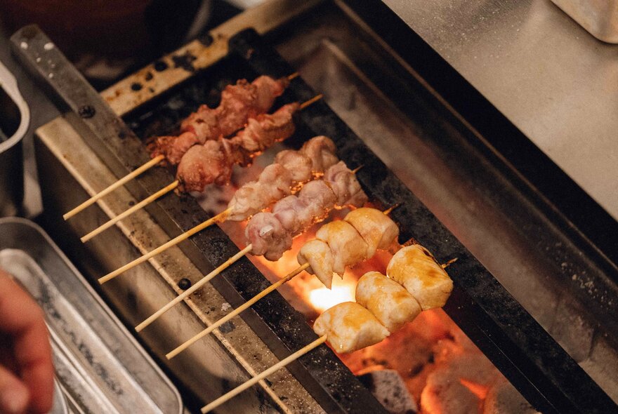 Japanese yakitori skewers cooking over a charcoal grill.