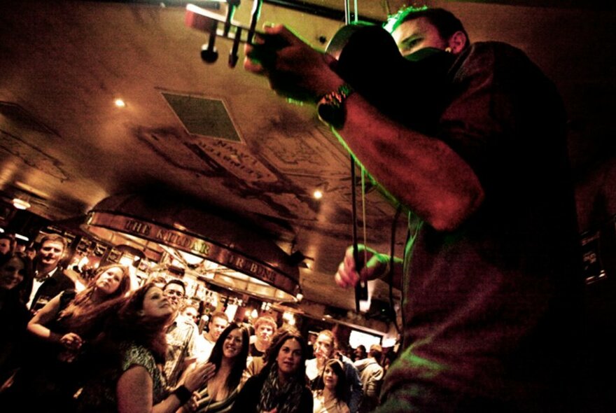 A fiddle player performing in a pub with people looking on.