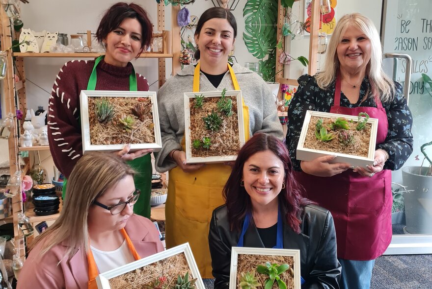 Five women holding up their succulent plant frames, four smiling and one looking down.