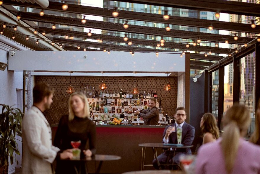 People at a rooftop bar talking and having a drink. 