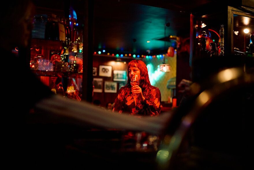 A dark bar with a woman in the distance raising a glass. 