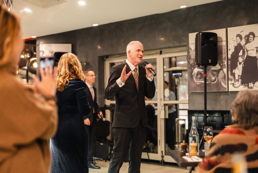 A man in a suit singing in a small space with people standing around him. 