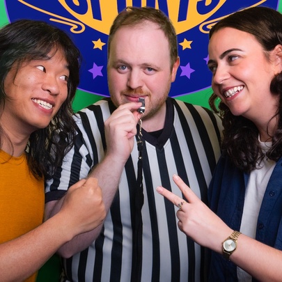 Two impro actors playing paper, scissors, rock either side of a pretend referee in a black and white striped shirt who holds a whistle.
