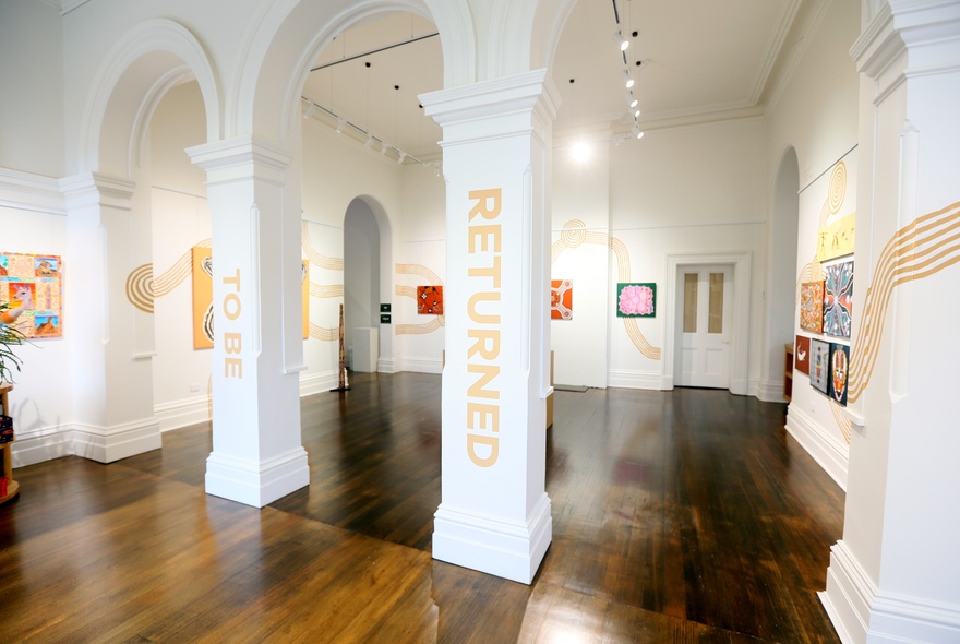 An arched gallery space with polished hardwood floors and First Nations artworks displayed on the walls.
