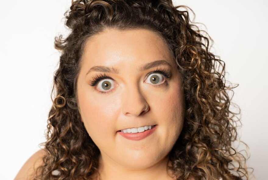 A close up of a woman's face showing her wide-eyed, biting her bottom lip.