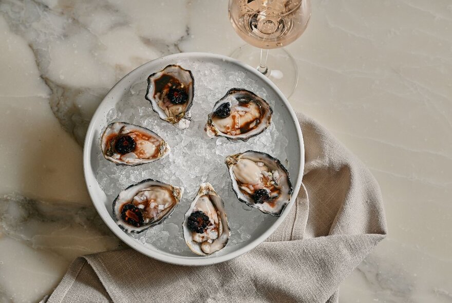 A plate of six oysters with a glass of rose.