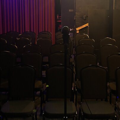 A dark image showing an empty theatre with rows of empty seats in front of a microphone on a stand.