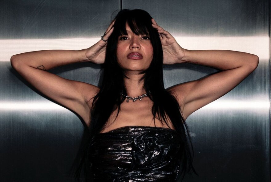 DJ and producer Zalina, her hands resting on either side of her head, wearing a strapless top, her long dark hair falling past her shoulders.