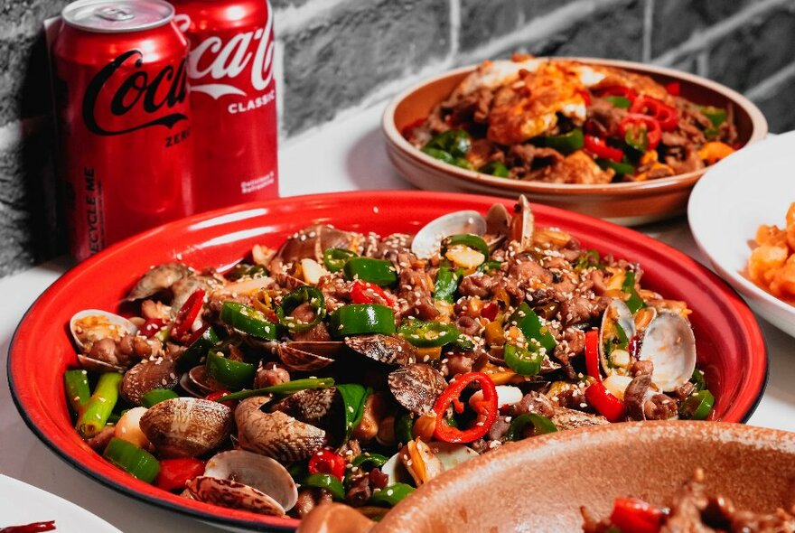 A Chinese stir fry with chillies and two cans of Coca Cola. 