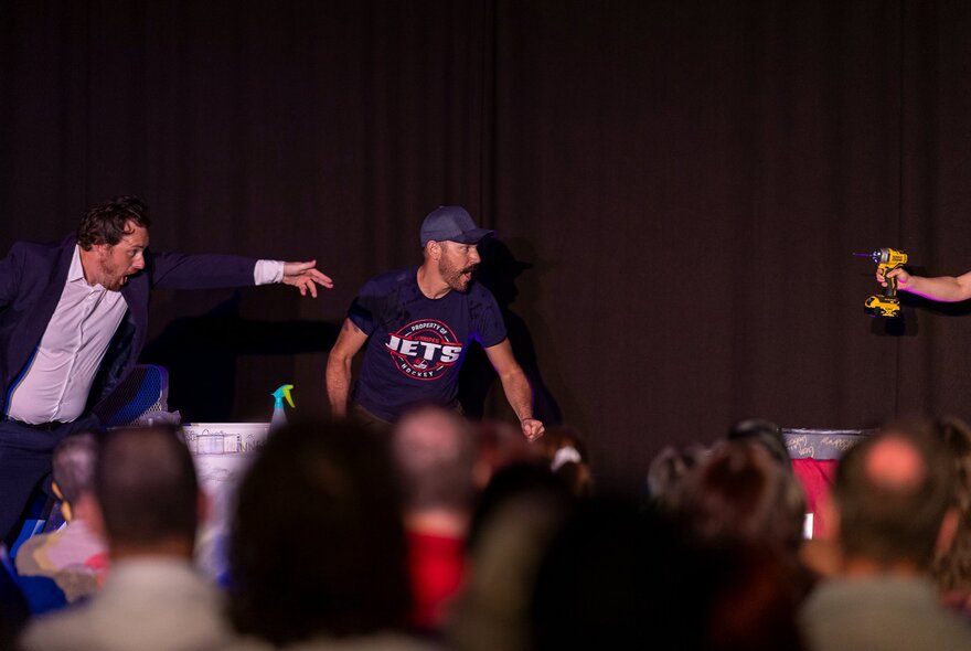 Performers on stage during a performance of the live comedy game show IKEA Wars, with the back of the heads of audience in the foreground.