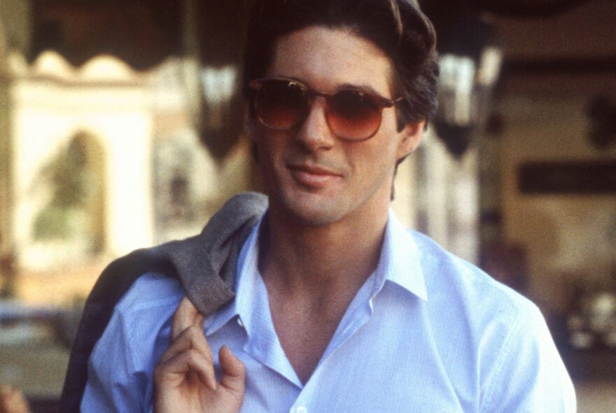 A scene from the film American Gigolo of actor Richard Gere wearing a white shirt with open neck, a jacket casually draped over his shoulder and sunglasses.