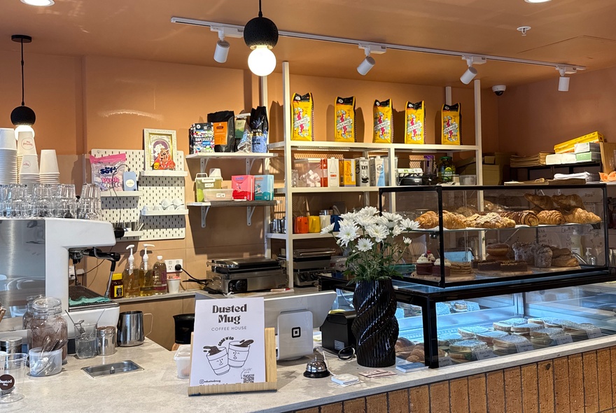 Cafe interior with pastries on display at front counter and products on shelves in the background.
