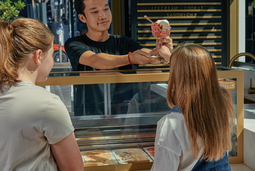 Vendor serving ice cream desserts to two customers, with ice cream counter.