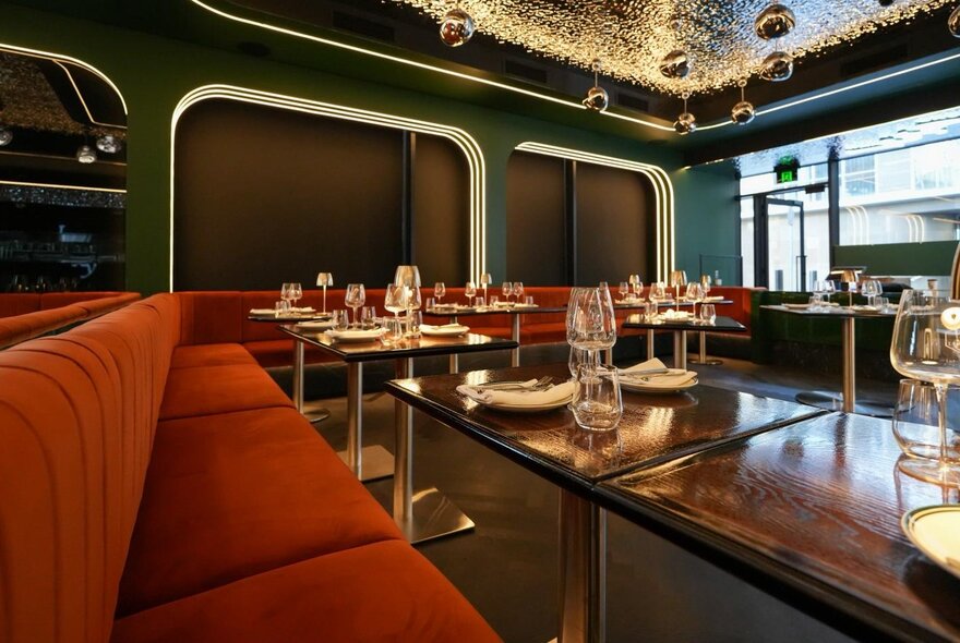Red banquettes with round tables set with glasses and napery in an Asian-inspired bar.